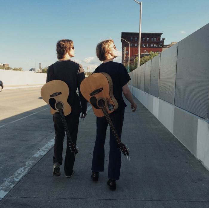 Two musicians walking with acoustic guitars slung on their backs