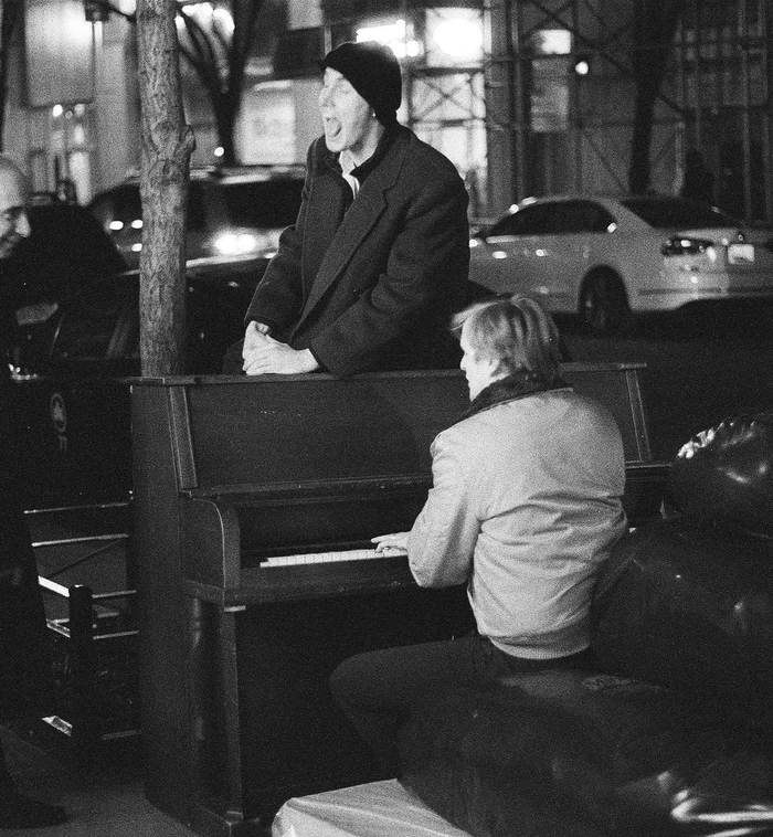 Singing atop an upright piano on a city street at night